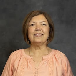 Smiling woman in a peach blouse against a dark studio background.